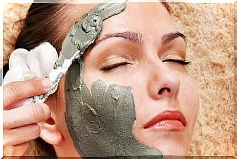 A woman applies a clay mask to her face